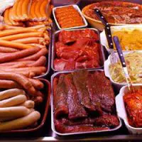 Auswahl an frischen Fleisch- und Wurstwaren mit verschiedenen Marinaden und Feinkostprodukten in einer Verkaufstheke.