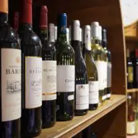 Verschiedene Rot- und Weißweinflaschen stehen ordentlich in einem Holzregal des Hofladens Bimöhlen.
